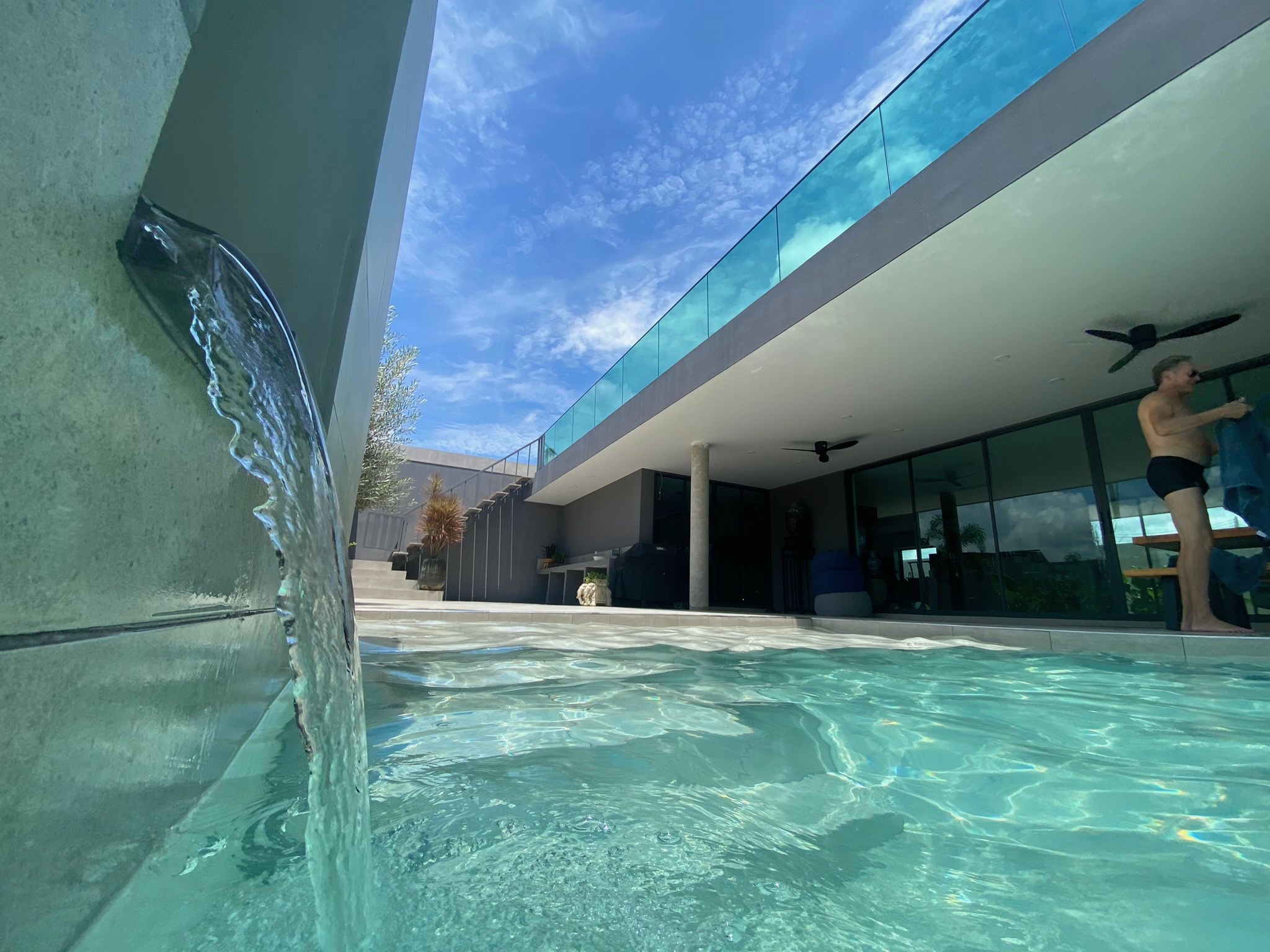 Close-up of pool waterfall feature with glass balustrade above
